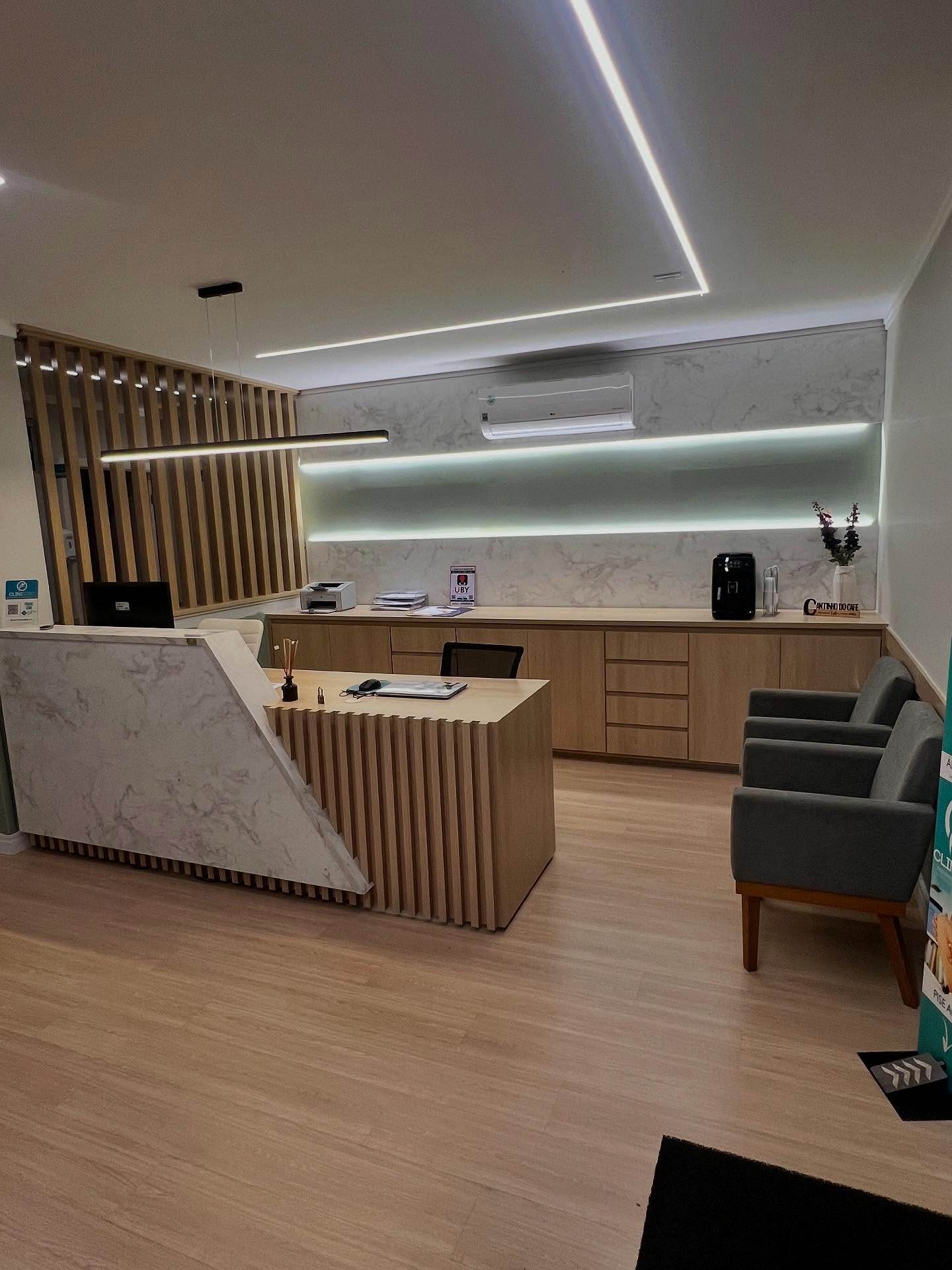 Recepção da Clinifisio com balcão ripado, bancada amadeirada e iluminação indireta