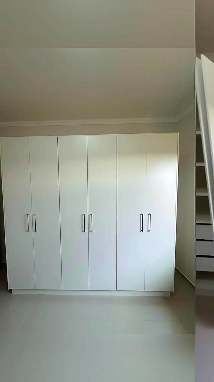 Guarda-roupa branco com portas de abrir ocupando a parede do quarto