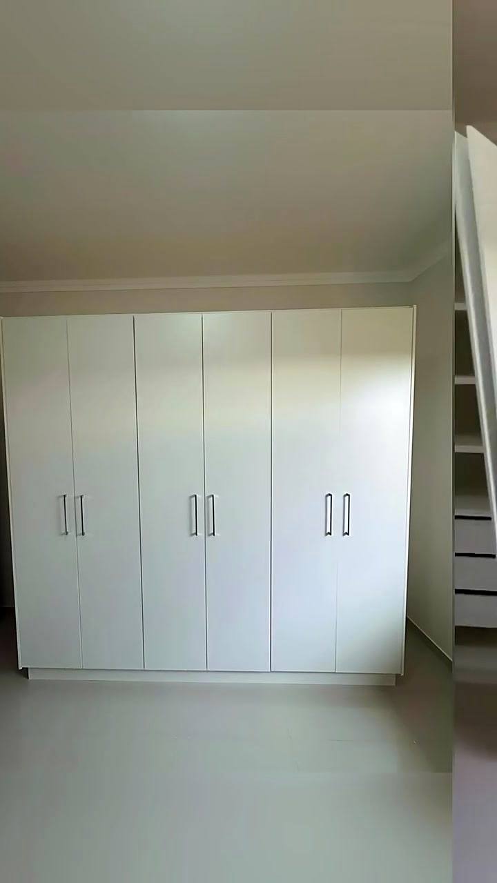Guarda-roupa branco com portas de abrir ocupando a parede do quarto